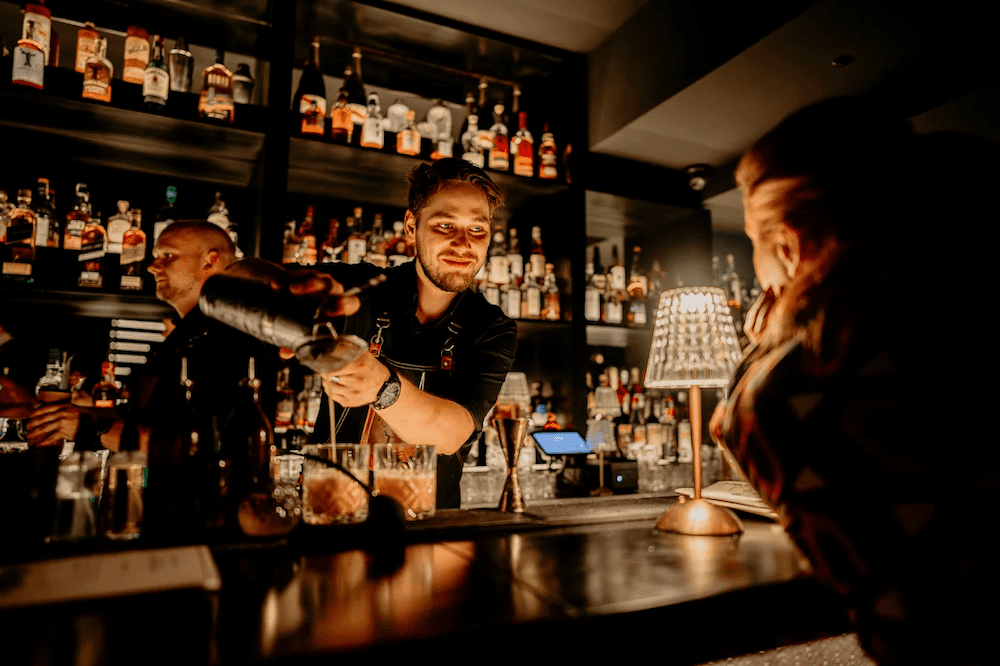 obrazek przedstawia barmana w trakcie pracy wpatrującego się kobietę pochylającą się nad ladą w jego kierunku