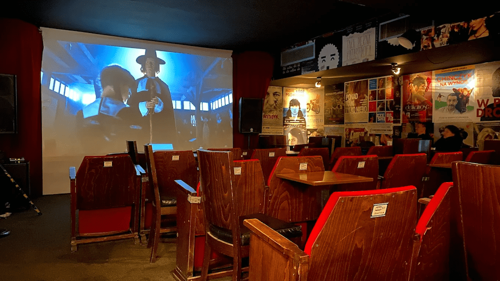 obrazek przedstawia wnętrze Ceski'ego Filmu ze Szczecina; wnętrze przedstawia rzutnik w trakcie transmisji oraz rzędy starych kinowych krzeseł