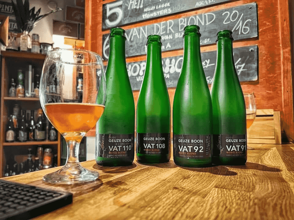 obraz przedstawia cztery zielone butelki piwa craftowego na drewnianym blacie oraz szklankę do piwa, napełniona około 1/3 cieczy