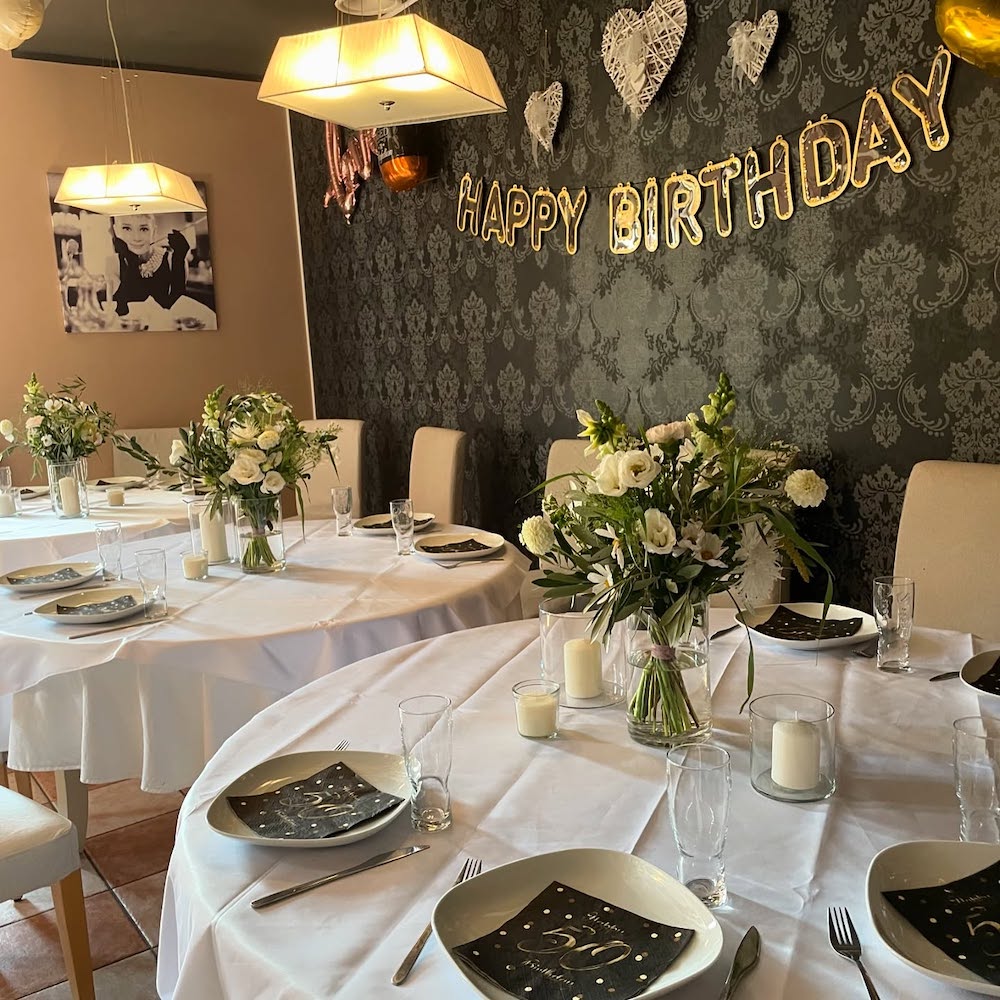 obrazek przedstawia wnętrze lokalu Fifty One w Szczecinie; stoły pokryte białymi obrusami, urozmaicone białymi bukietami oraz świecami i zastawą;