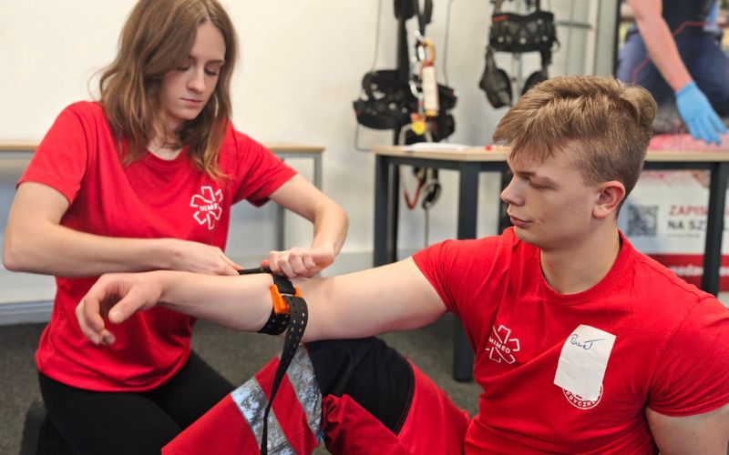 Zdjęcie przedstawia dwie osoby na szkoleniu Stop The Bleed, które uczą się używać opaski uciskowej