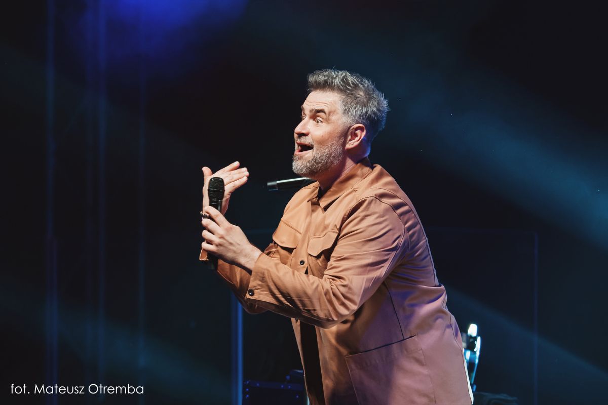 Zdjęcie przedstawia Igora Kwiatkowskiego na scenie podczas wykonywania stand-upu
