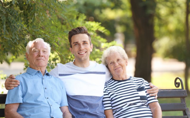 Zdjęcie przedstawia parę emerytów wraz z wnukiem, który ich obejmuje na ławce