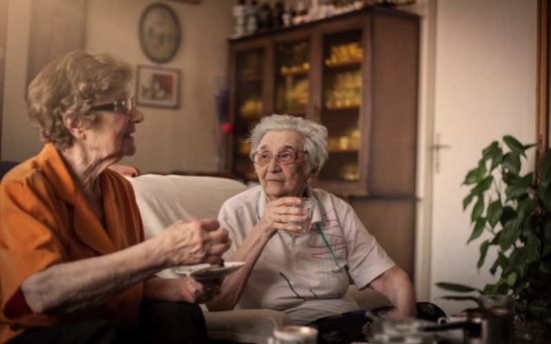 Zdjęcie przedstawia dwie kobiety na emeryturze, które siedzą na kanapie