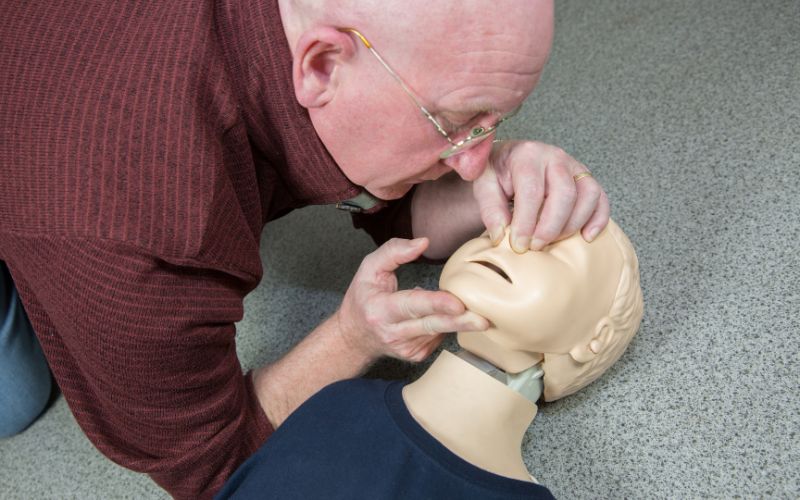 Zdjęcie przedstawia mężczyznę, który ćwiczy resuscytację na fantomie