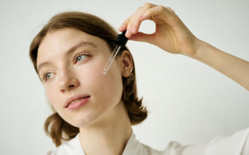 Zdjęcie przedstawia kobietę, która przykłada pipetę z serum do twarzy
