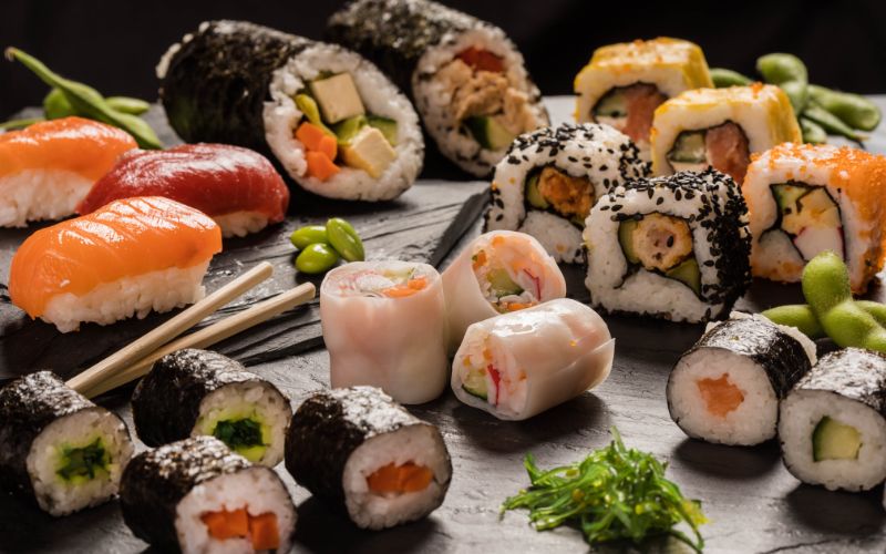 Zdjęcie przedstawia ozdobną deskę, na której poukładane są różne rodzaje sushi
