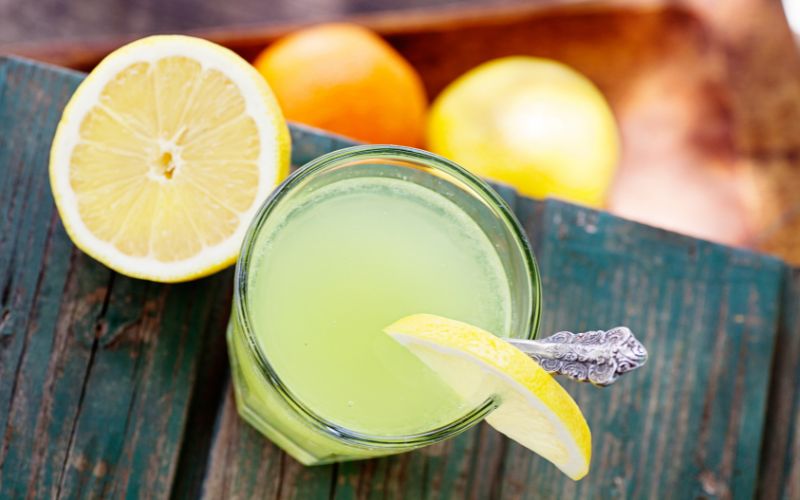 Zdjęcie przedstawia lemoniadę na stole drewnianym, gdzie leżą cytryny