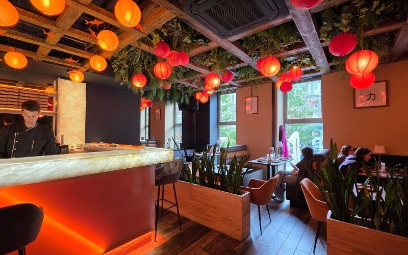 Wnętrze restauracji SAME sushi & robata w Szczecinie z oświetlonymi stolikami oraz widokiem na Sushimastera